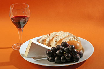 french bread, brie cheese, a bunch of grapes, and a glass of red wine
